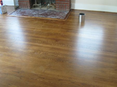 Medium-brown oak hardwood floor with a glossy refinished sheen beside a brick fireplace in a Houston home